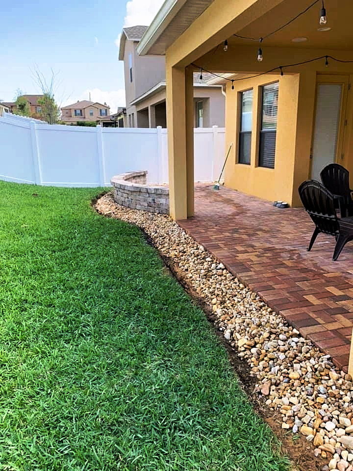 Backyard transformation with new paver patio edge, stone seating wall, river rock border and fresh sod